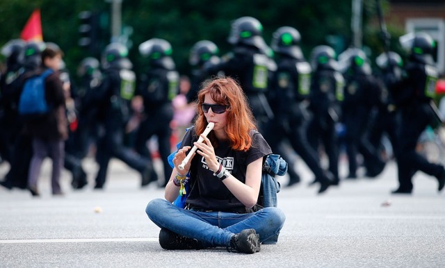 Manifestante toca flauta enquanto polícia passa durante protesto contra a realização do G20, nesta sexta-feira (7) (Foto: Hannibal Hanschke/ Reuters)