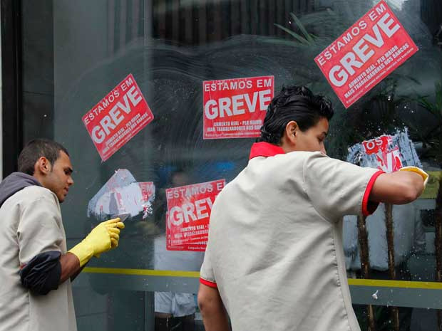 Funcionários retiram adesivos  colocados nas portas e paredes de agência em SP (Foto: FuturaPress)