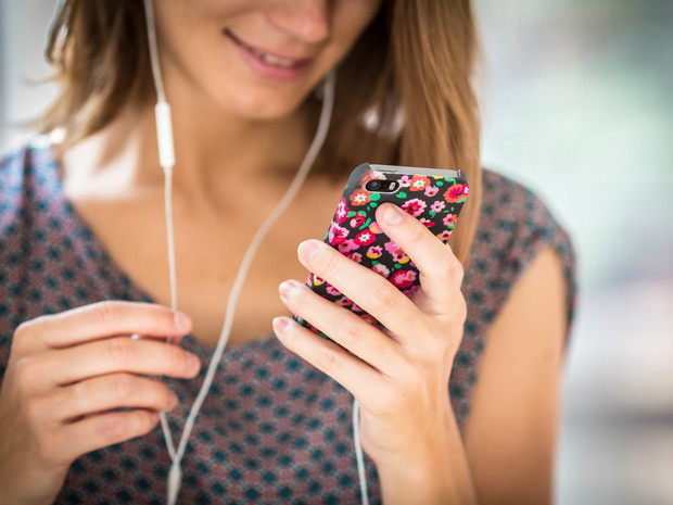 Mulher utiliza seu smartphone com fones de ouvido (Foto: GARO/Phanie)